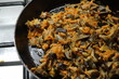 Onions, carrots and oyster mushrooms are passioned in a frying pan on a gas stove.
