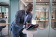© FotoArtist - Portrai of African American businessman using  laptop of mobile device  in modern office.