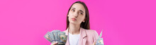 A Woman In A Pink Jacket Holds Dollar Banknotes, A Puzzled Business Girl Hides Dollars Standing On A Red Background.