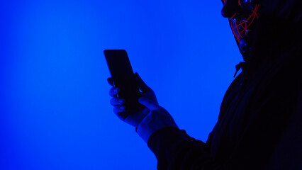 Anonymous hacker and face mask with smartphone in hand. Man in black hood shirt trying to hack personal data from mobile phone. Represent cyber crime data hacking or personal data stealing concept.