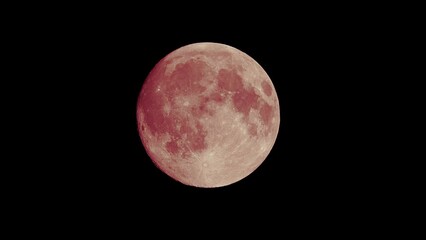 red full moon on dark black sky background, shot from surface of earth with very long telephoto lens
