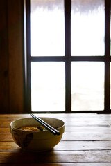 Bowl of hot instant ramen noodles on a table next to a window