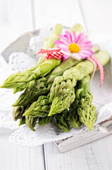 Fresh raw green asparagus bundle offered as close-up on wooden white tray