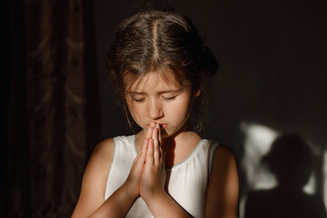 A little girl folded her hands in prayer in the hope of ending the war in Ukraine, a Ukrainian child prays and believes in a happy future