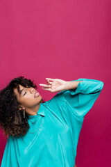 Wall Mural - african american woman in blue blouse posing with hand near face and looking up isolated on pink.