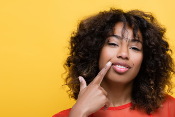 Wall Mural - cheerful african american woman pointing with finger at own smile isolated on yellow.