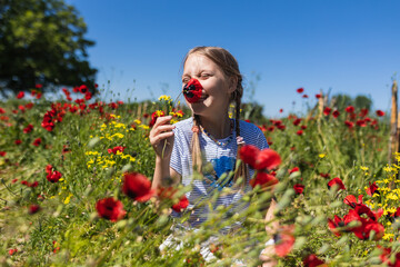 A smiley girl holding poppy flower in her hand and smelling it in the poppy field. Lifestyle concept.