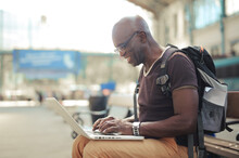 Portrait Of Man On A Bench In Train Station While Using A Computer