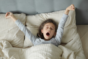 cute little girl stretches in bed when she wakes up