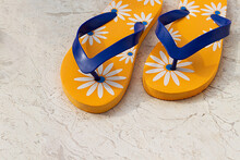 Yellow Women's Beach Slippers With A Pattern Of Flowers On A Stone Background. National Flip Flops Day Concept.