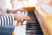 Close Up Of A Little Student's Hands Is Playing, Learning And Practicing The Piano. Music Abilities For Kids. Hobby And Activity For The Children. Hand Of An Experienced Pianist Helping Young Student.