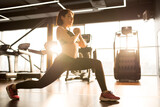 Fototapeta  - Young slim woman in sports clothing concentrating on her exercises, she doing lunges alone in health club