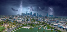 An Aerial Panoramic Of The Skyscrapers And Office Buildings In The City Skyline And A Green Lake With Lush Green Palm Trees And Grass With Cars Driving On The Street And  Storm Clouds With Lightning