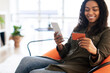 © Prostock-studio - Smiling black lady using phone and credit card at home