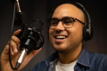 Wall Mural - Young asian man host streaming podcast with condenser microphone work on laptop at small broadcast home studio. Content creator blogger recording voice over radio interview guest conversation