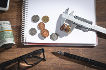 Wall Mural - Vernier caliper, dollar banknotes, pen, eyeglasses, coins, notepad on the wooden table.