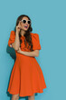 Beautiful young woman in orange cocktail dress and sunglasses is looking away and laughing.