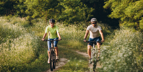 A man and a woman ride bicycles on a dirt road in the summer at sunset. Active rest in the summer on bicycles.