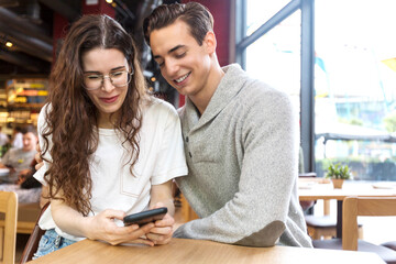 Título: Smiling couple at cafe using mobile phone