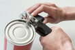 Hands opening a can in a kitchen with a tin opener.