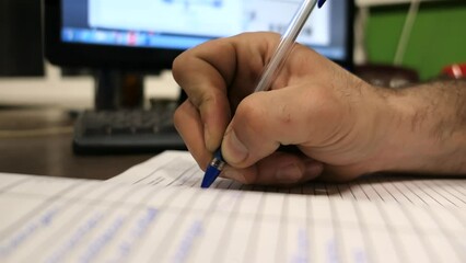 a hand of a man making notes in a notebook with a computer on a background and it takes place on a factory 