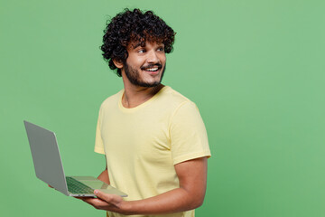 Sticker - Young happy Indian man 20s in basic yellow t-shirt hold use work on laptop pc computer look aside on workspace isolated on plain pastel light green background studio portrait People lifestyle concept