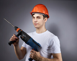 a young construction worker in a hard hat and a white T-shirt with a puncher in his hand.