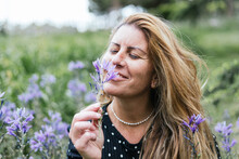 Mature Blonde Woman Smelling A Violet Flower In Spring. Relaxing Concept In Nature.