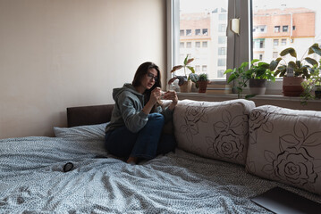 Young nervous woman is sitting at home holding a pregnancy test and is impatiently waiting for the test result. Maybe pregnant maybe not concept