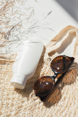 Wall Mural - Plastic white tube for cream or lotion with sunglasses and loth shopping bag. Sunscreen cosmetic on white background with beautiful shadows and field grass. Beauty summer concept for face care