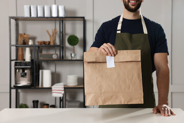 Canvas Print - Worker with paper bag at counter in cafe, closeup. Space for text