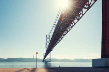 Wall Mural - 25th April Bridge on Tejo river in Lisbon, Portugal. Summer cityscape. View of promenade in the morning sunlight