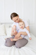© Any Grant - a mother with a baby in her arms gently hugs a smiling child on the bed at home