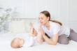 © Any Grant - happy mother with baby playing with his legs on the bed at home
