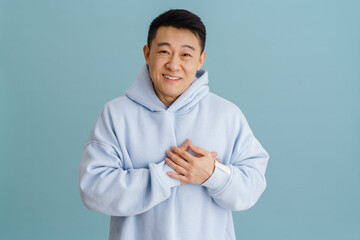 Wall Mural - brunette adult asian man smiling and keeping hands on his heart