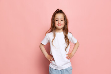 studio shot of cute little girl, kid wearing white t-shirt posing isolated on pink background. conce