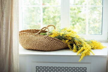 Wall Mural - Bouquet mimosa flowers in wicker basket near window. Flowers mimosa in basket on windowsill. Beautiful yellow spring flowers. 8 March , Easter, Mother's day. Branches yellow mimosa in a bouquet.	
