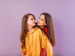 Wall Mural - Happy smiling beautiful young mother and cute daughter posing in fashion trendy bright colorful hoodie together on purple studio background with empty copy space. Happy