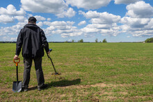 Treasure Hunter. Man With Metal Detector. Human Search Treasure On Green Field. Guy With Metal Detector And Shovel. Treasure Hunter With His Back To Camera. Concept Of Archaeological Excavations