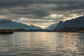 Wall Mural - Norwegian seascape, lighthouse on the island, rocky coast with dramatic skies, the sun breaks through the clouds, sheer cliffs, small islands illuminated by the sun