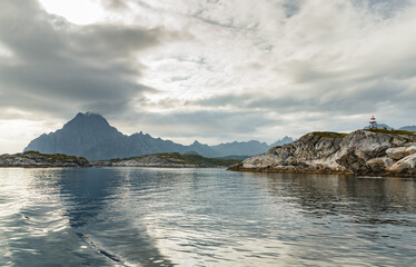 Wall Mural - Norwegian seascape, lighthouse on the island, rocky coast with dramatic skies, the sun breaks through the clouds, sheer cliffs, small islands illuminated by the sun