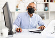 Professional business man in protective medical mask using laptop at workplace in office