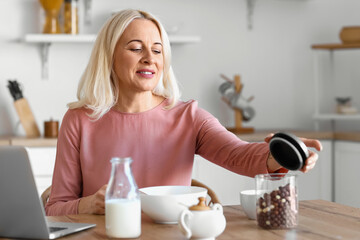 Wall Mural - Morning of mature woman having breakfast in kitchen