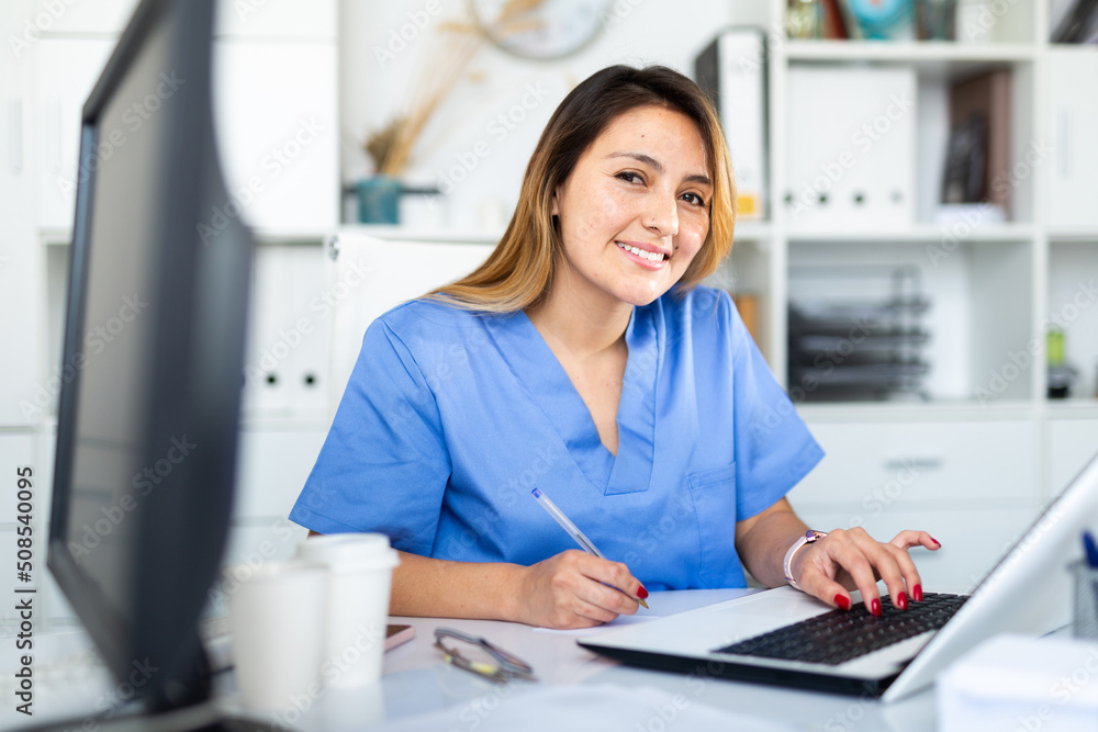 Young hispanic woman doctor assistant working in medical office using ...