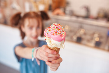 Wall Mural - Cute little girl eating ice cream in cafeteria. Child holding icecream. Kid and sweets