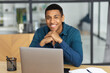 © kucherav - Portrait of successful African American young male sitting in modern office using laptop for work looks at the camera and smiles friendly