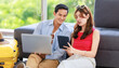 © Bangkok Click Studio - Asian young lovely boyfriend and girlfriend traveler couple sitting smiling on carpet in living room with trolley luggage while using laptop computer and tablet booking vacation summer trip online