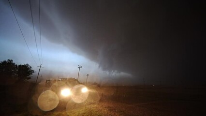 Wall Mural - Dangerous thunderstorm moving in at night as it rains and wind blows looking at car with headlights on.