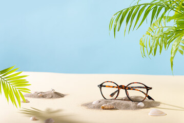 Trendy Eyeglass frame on a beach with palm leaves, trendy Still Life Style. Tortoiseshell frame glasses on sand. Summer Optic store advertisement background. Copy space. Glasses sale concept. Eyeweare