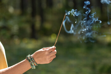 occult science and supernatural concept - close up of hand with smoking incense stick performing magic ritual in forest